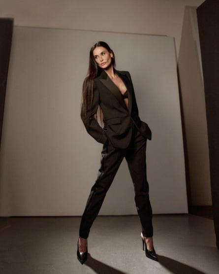 Portrait of Demi Moore in  tuxedo jacket, straight leg jeans and very high heels, standing in a power pose