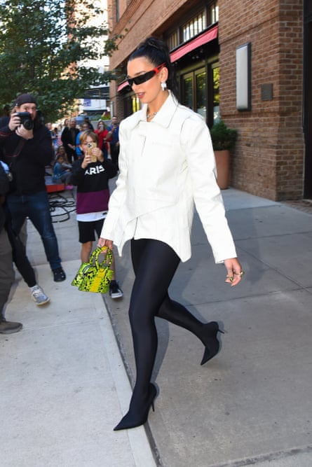 Pop star Dua Lipa is photographed in New York City in September 2022. She is wearing black leggings and a white shirt and carrying a green and yellow snake printed Ana bag from Luar. 