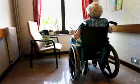 woman with grey hair in wheelchair in small room looking out window