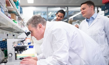 Keir Starmer looking at a cancer tumour under a microscope during a visit to the Francis Crick Institute in north London this morning, with Wes Streeting (right) looking on.