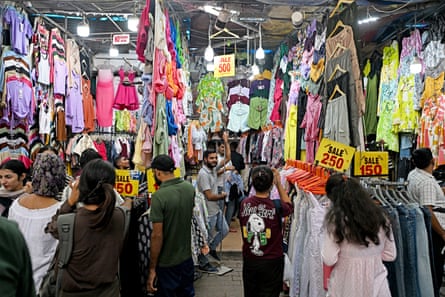 S crowded and brightly lit market with clothes hanging up on display alongside large labels advertising low prices.