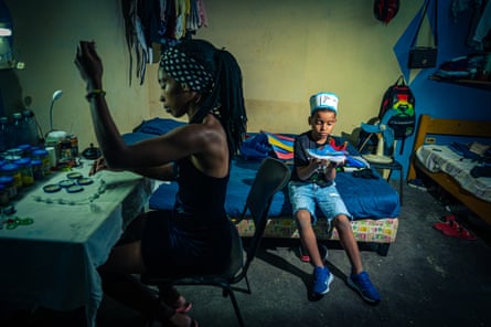 Artelis, 31, makes religious jewellery in the shelter while her son Bryan, 7, holds the trainers his father sent from the US