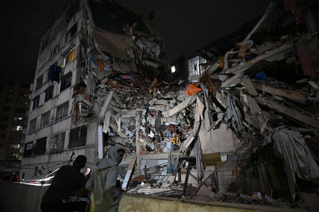 People look at a collapsed building in the dark