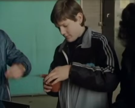 A teenage boy in a tracksuit top holds an indistinct brown object.