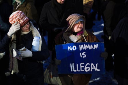 a person holds a sign that reads ‘no human is illegal’