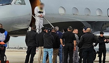 A man in handcuffs, who face has been pixellated walks down steps from a jet