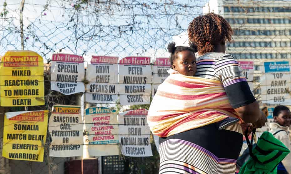 A woman carrying a child walks past newspaper headlines on a street in Harare, 7 September 2019.
