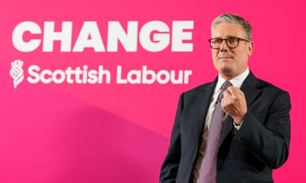 Keir Starmer, in a shirt, suit and jacket, wearing glasses and looks serious holding his left fist before him in front of a sign reading “Change: Scottish Labour”