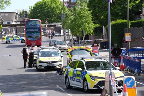 Police officers stand near a line of police vehicles in a cordoned area at the scene in Golders Green.