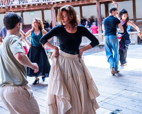 A woman in a black top and beige tiered skirt dances with others in a bright studio space. Love’s Labour’s Lost rehearsals in Shakespeare’s Globe.