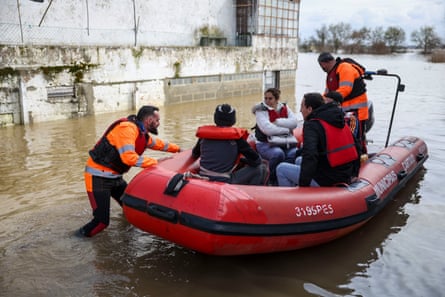 People wearing life jackets in dinghy on flooded street.