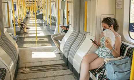 A passenger on the tube in London uses a fan to cool down from the heat and humid conditions during the current heatwave