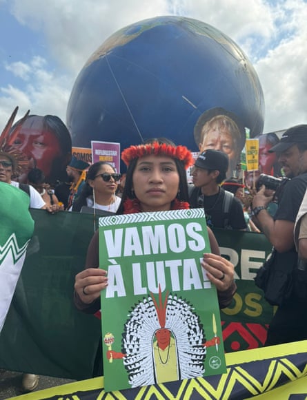 Raquel Wapichana with a flower band around her head, holds up a sign that says ‘Vamos a Luta!’