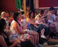 Women holding babies watching a performance - some of them are laughing and some are tending to their children.