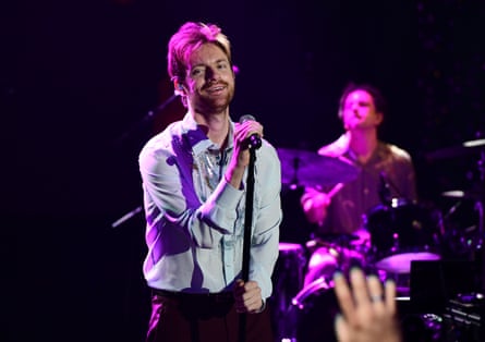Man with a blue shirt performs on a stage bathed in pink light