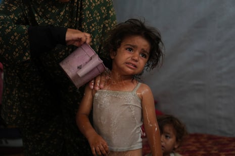 Rida Abu Hadayed, 32, cools off her two-year-old daughter Azhar with water in their tent at a camp for displaced people in Khan Younis, southern Gaza Strip.