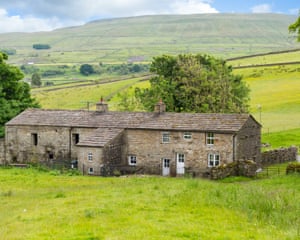 A low two-storey stone building nestling within the green farmland and rolling hills