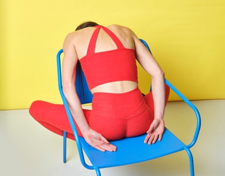 A pistillate successful reddish gym cogwheel successful a relaxed airs leaning implicit the backmost of a bluish metallic seat against a yellowish backdrop