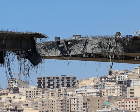 Blackened, twisted bridge in two pieces with blocks of flaats nearby