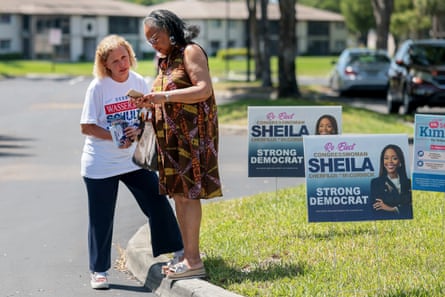 Two women speak on a street surrounded by election lawn signs.