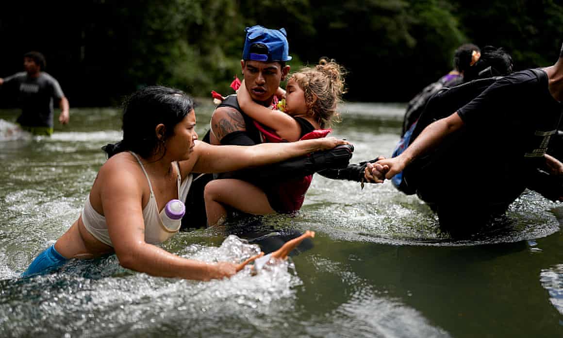 A child is carried as people wade across a river