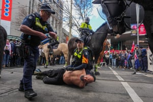 A police officer holds a bare-chested man on the ground surrounded by other officers on horseback