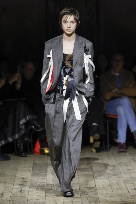 A model walks the Simone Rocha runway in an oversized grey pinstripe suit with white ribbons