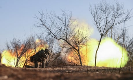 A Ukrainian artillery operator crouches with ears covered as a howitzer is fired, shooting out flames, on the frontline in the Zaporizhzhia region