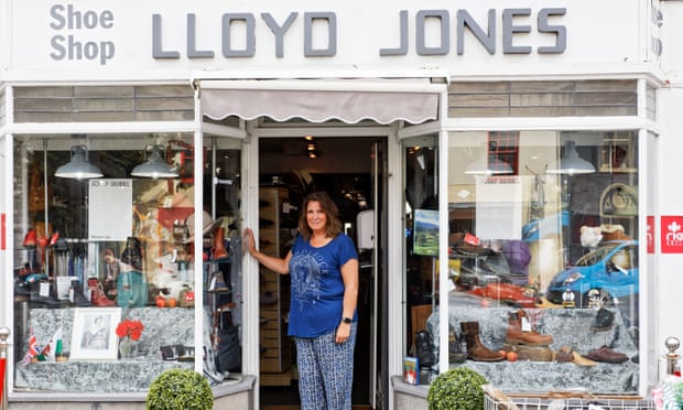 Judith Williams in her shop door with portrait of Queen in window.