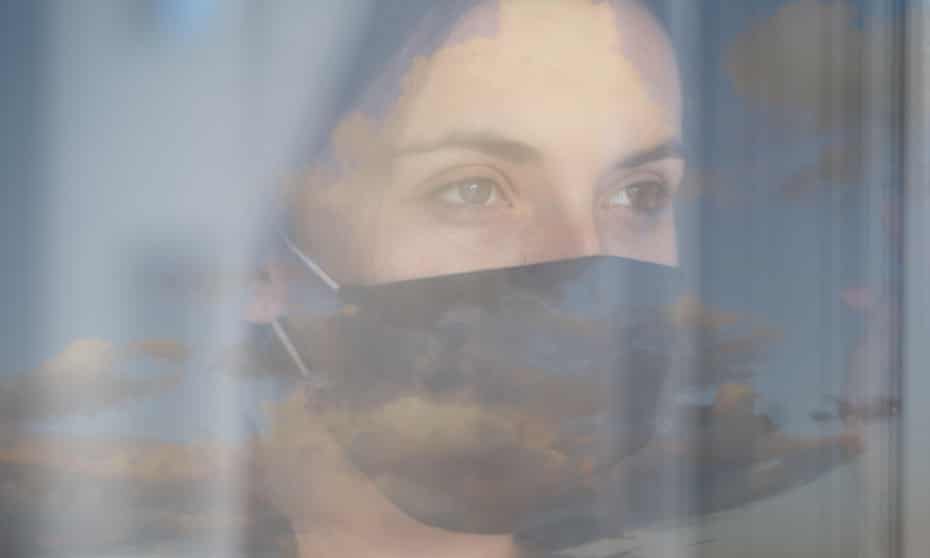 woman looking through net curtains in mask