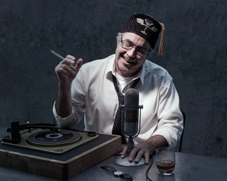 Danny Baker at Shorditch studios with a record deck and a microphone in front of him, smiling/laughing