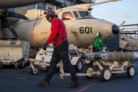 A sailor wheels munitions in front of a plane.