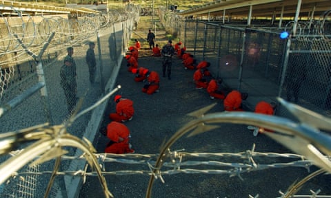 Detainees in orange jumpsuits sit in a holding area at Camp X-Ray at Guantánamo Bay on 11 January 2002. 