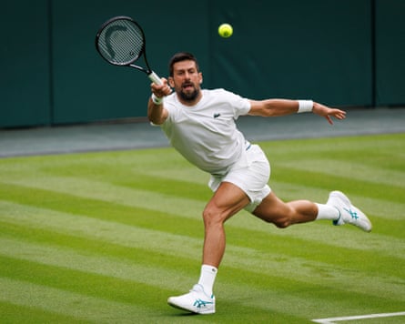 Novak Djokovic wearing white tennis gear stretches for a forehand on the grass courts at Wimbledon