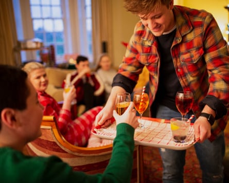 One young man is serving drinks to his friends at a Christmas house party.