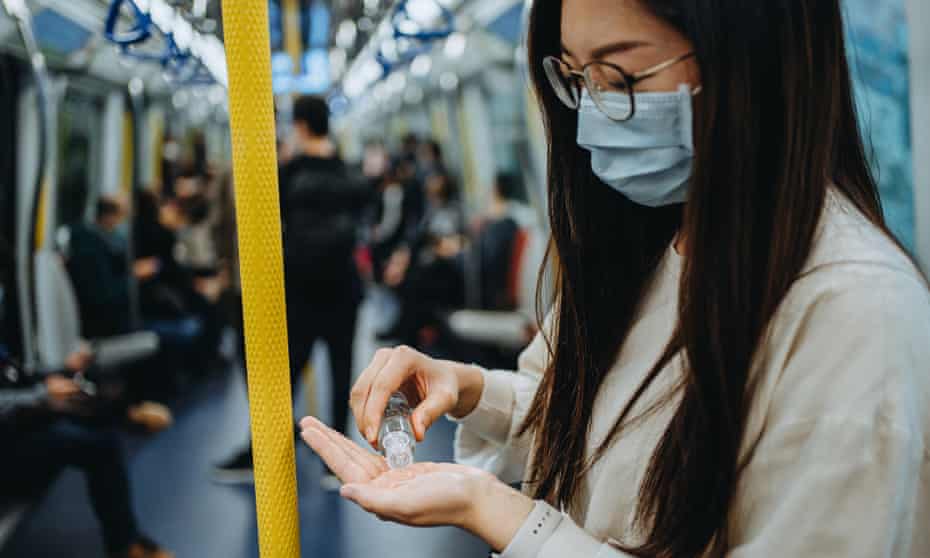 A young woman on public transport wearing a mask and sanitising her hands
