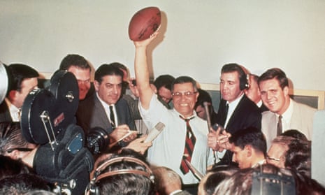 Green Bay Packers coach Vince Lombardi raises a football in victory, surrounded by reporters covering the first Super Bowl in 1967.