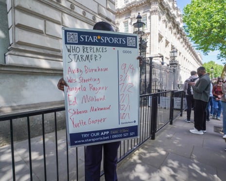 A man stands with a board outside Downing Street reading Who replaces Starmer, and odds for Andy Burnham (9/4), Wes Streeting (3/1), Angela Rayner (7/2), Ed Miliband (7/1) and others