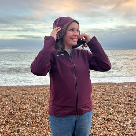 A woman on a pebble beach on a cloudy day tests waterproof jackets.