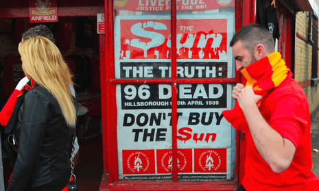 People outside Liverpool FC's stadium walk past a poster that is a mockup of a Sun newspaper billboard which has blood dripping from the masthead and includes the words 'Don't buy the Sun'