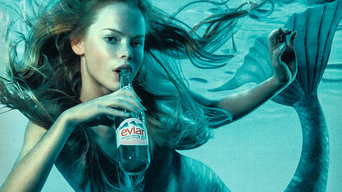 A mermaid sips from an Evian bottle