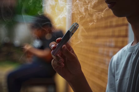 Asian male teenager holds a smoked e-cigarette in his hand in a hidden corner with his friends at school