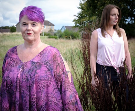 Wendy photographed in the foreground, looking at the camera, with Laura a few steps behind her, looking to her left, both standing in a field with houses in the background