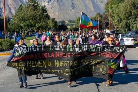 A group of women walk down a road holding a large banner before them.