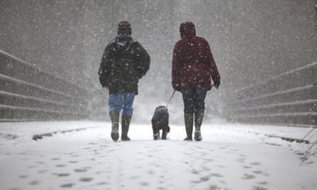 Two dog owners walk through snow with their dog in Crawley, England