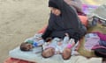 Woman in a hijab trying to feed three tiny babies with bottles in a tent.