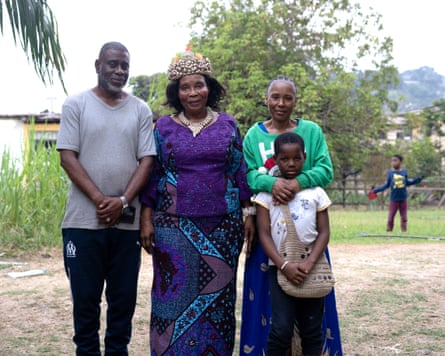 A man, two women and a boy pose outside for a photo. Another boy can be seen in the distance behind them