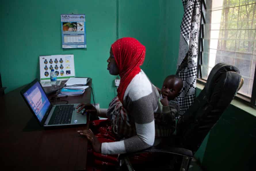 Holding her 11-month-old son, Ibrahim, securely wrapped in a cloth around her back, Fatou Ceesay, 33, works in her office near her home in rural Soma, in central Gambia.