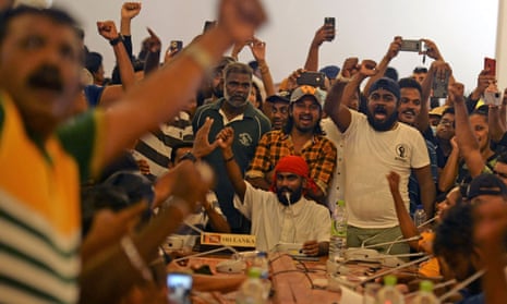Crowd of people gather around central table; some hold up mobile phones to take photographs
