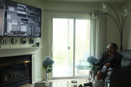 man watches tv screen in living room. tv is over a fireplace, and a glass door is in the back